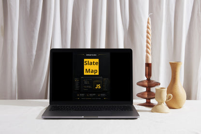 A black laptop displaying the Slate Map JS dashboard, styled on a white surface with decorative ceramic vases and a tall spiral candle holder against a draped white curtain background.